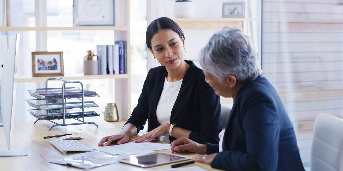 Two women discussing documents at desk.